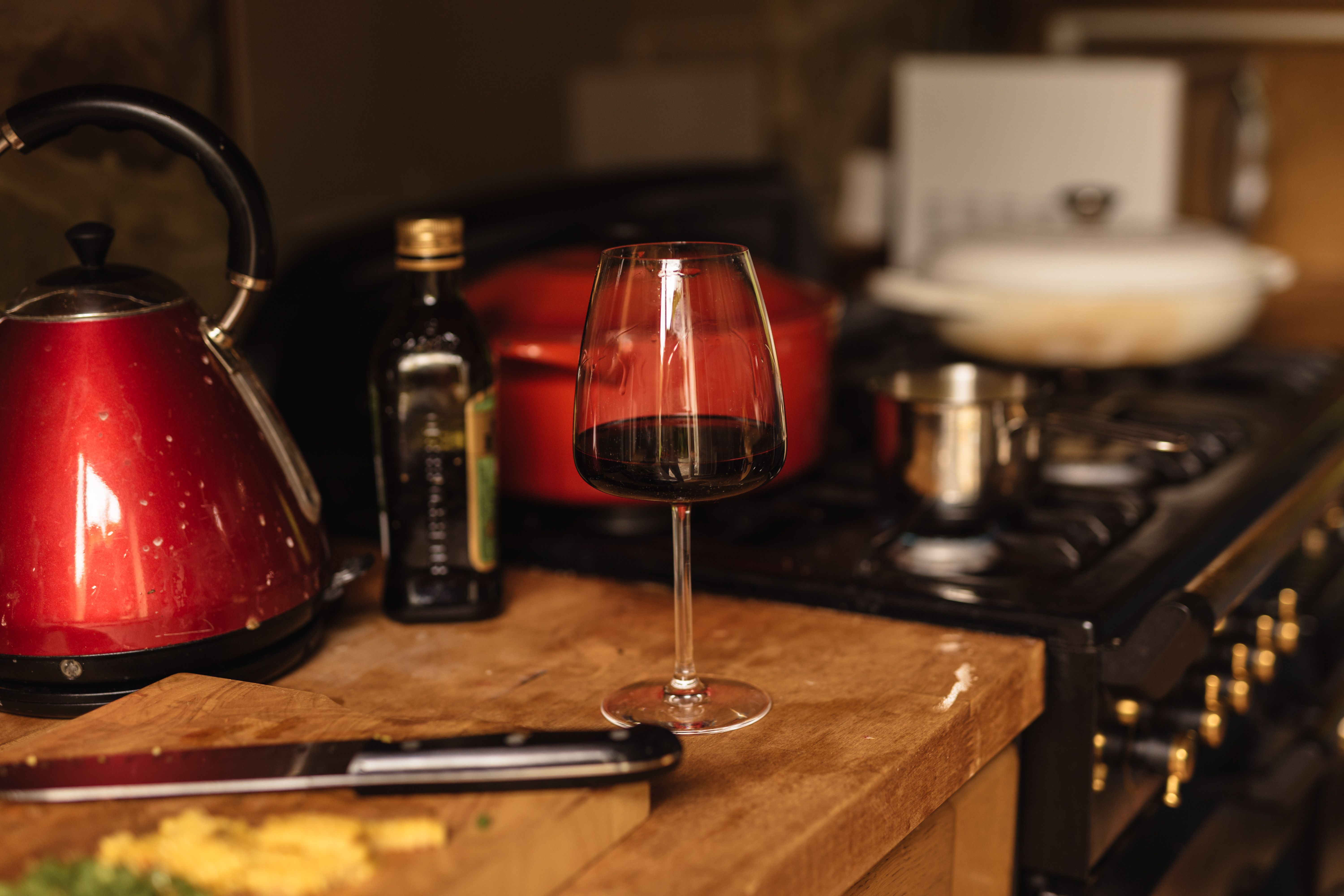 A wine glass on a kitchen counter with a red kettle and cutting board. Image: Olga Lioncat/Pexels 