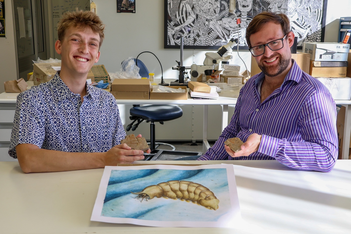 Thomas Turner (left) and Dr Russell Bicknell (right) with Turner's illustration of the 500-million-old anthropod Magnicornaspis garwoodi. - Image provided by Flinders University