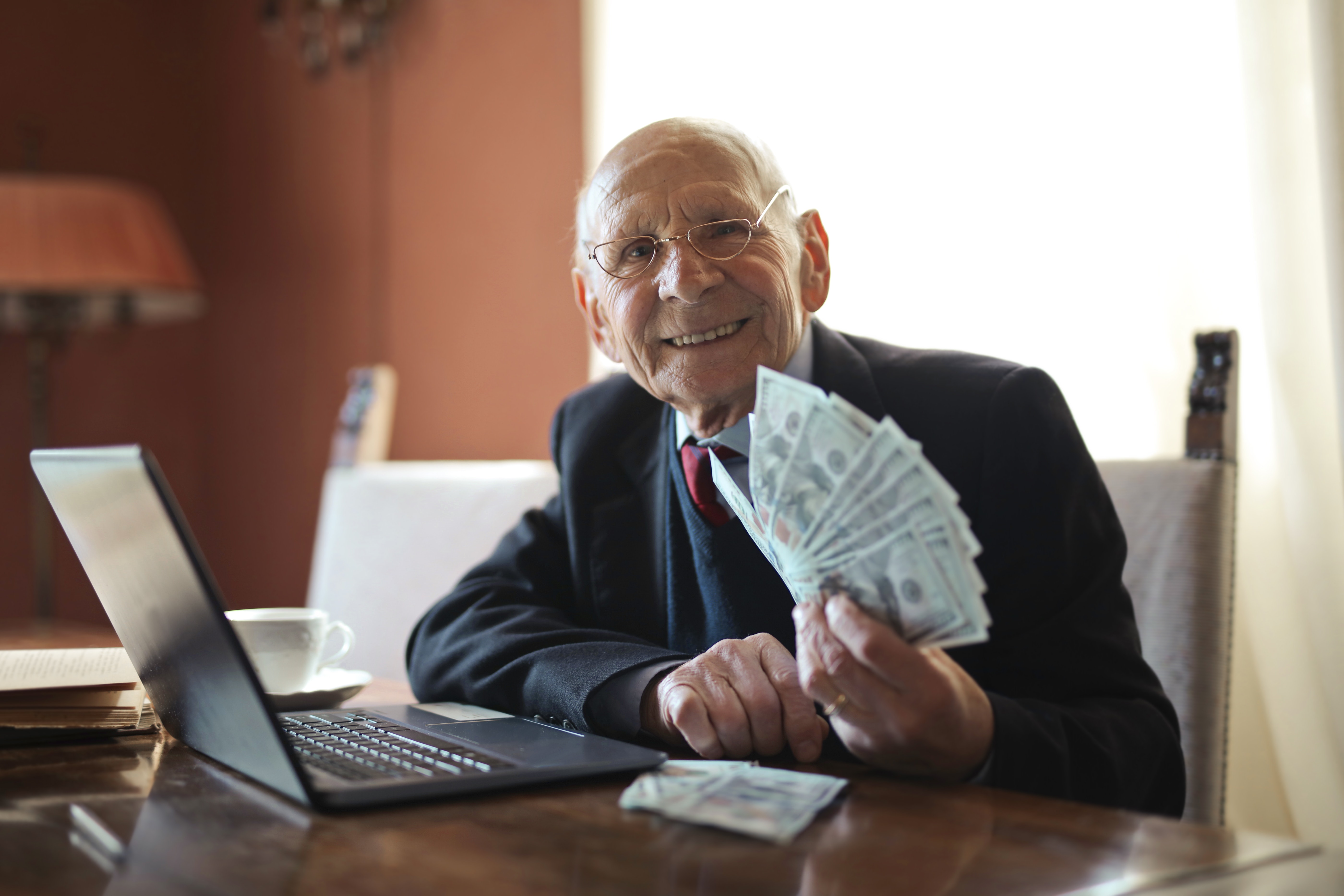 CC-0. Andrea Piacquadio on Pexels: https://www.pexels.com/photo/happy-senior-businessman-holding-money-in-hand-while-working-on-laptop-at-table-3823487/