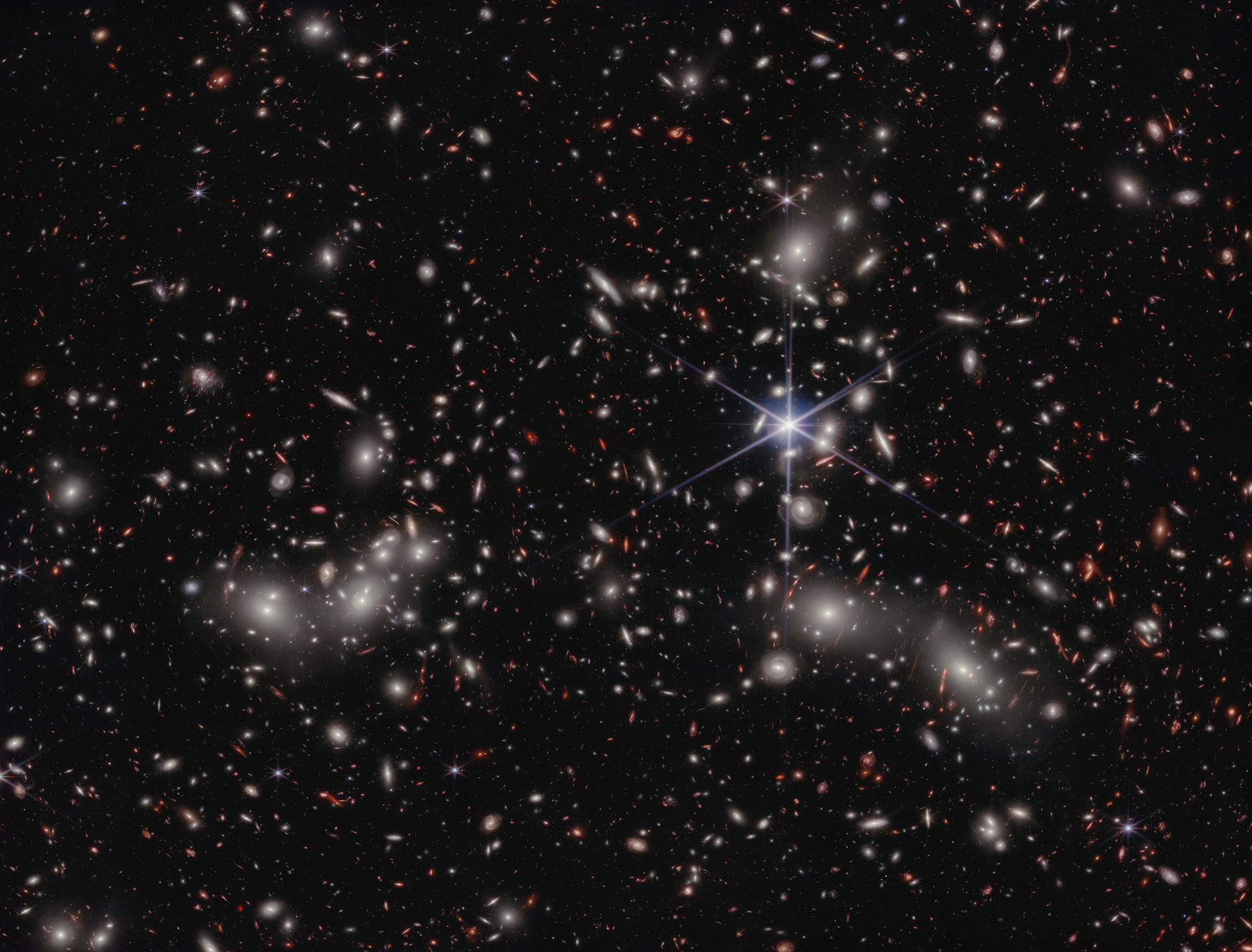 Astronomers estimate 50,000 sources of near-infrared light are represented in this image from NASA’s James Webb Space Telescope. Their light has travelled through varying distances to reach the telescope’s detectors, representing the vastness of space in a single image. A foreground star in our own galaxy, to the right of the image center, displays Webb’s distinctive diffraction spikes. Bright white sources surrounded by a hazy glow are the galaxies of Pandora’s Cluster, a conglomeration of already-massive clusters of galaxies coming together to form a megacluster. The concentration of mass is so great that the fabric of spacetime is warped by gravity, creating a natural, super-magnifying glass called a “gravitational lens” that astronomers can use to see very distant sources of light beyond the cluster that would otherwise be undetectable, even to Webb.    Credit: NASA, ESA, CSA, I. Labbe (Swinburne University of Technology) and R. Bezanson (University of Pittsburgh). Image processing: Alyssa Pagan (STScI) 