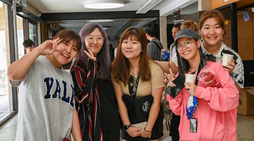 Five female university students smiling and giving the peace sign.