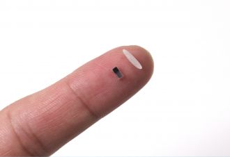 A pacemaker sits next to a single grain of rice on a fingertip.